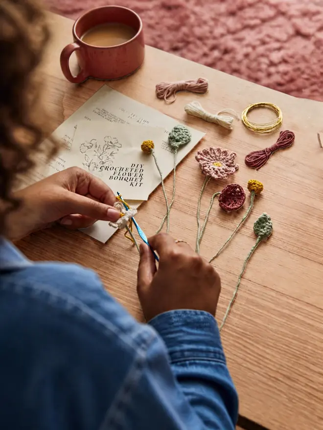 hands making a crocheted flower posy at table