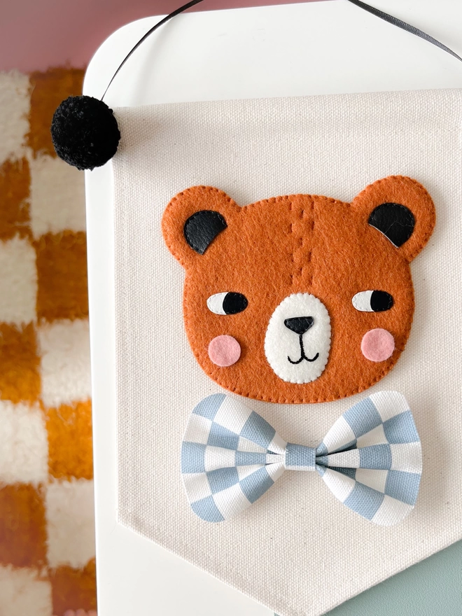 Brown bear hand sewn banner with a blue chequered bow tie on a cream fabric background