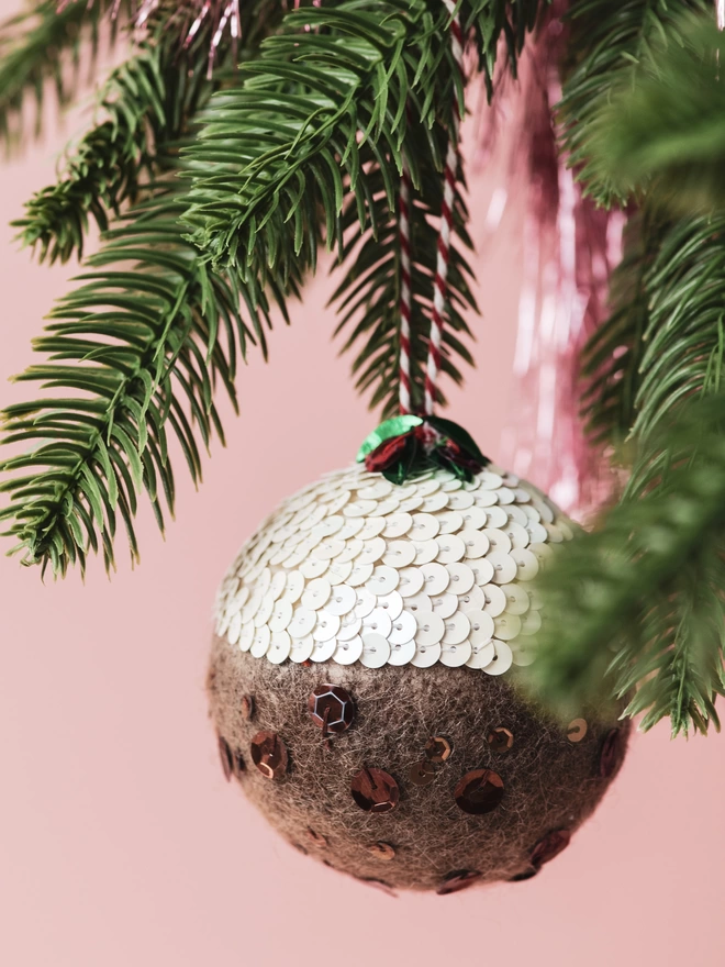 A sequinned Christmas Pudding ornament hanging on a tree