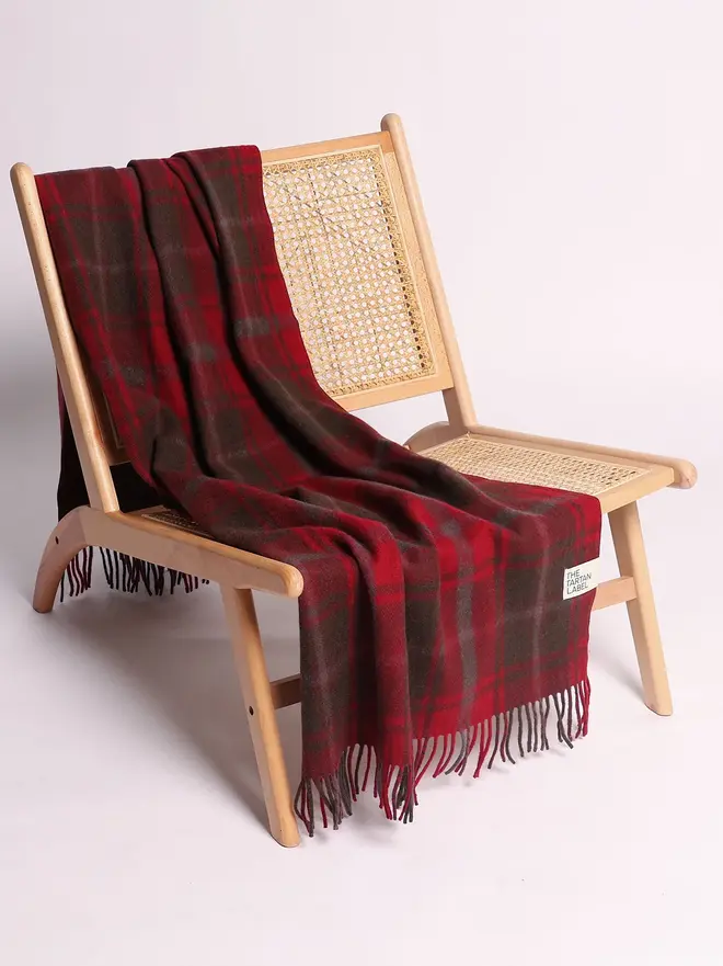 Dark Maple Tartan Blanket, a red blanket draped over a wooden chair on a white surface against a plain backdrop. 