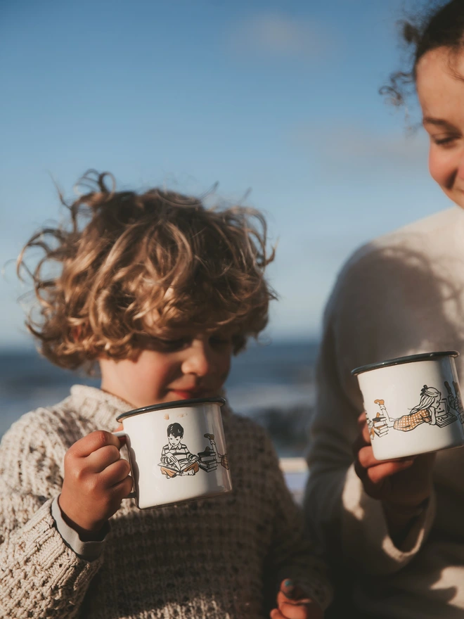 children holding cream illustrated enamel mugs on a beach