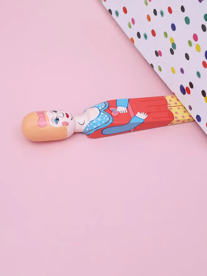 Wooden Door Stopper (Pez), a colourful wooden door stop sitting on a pink surface. 