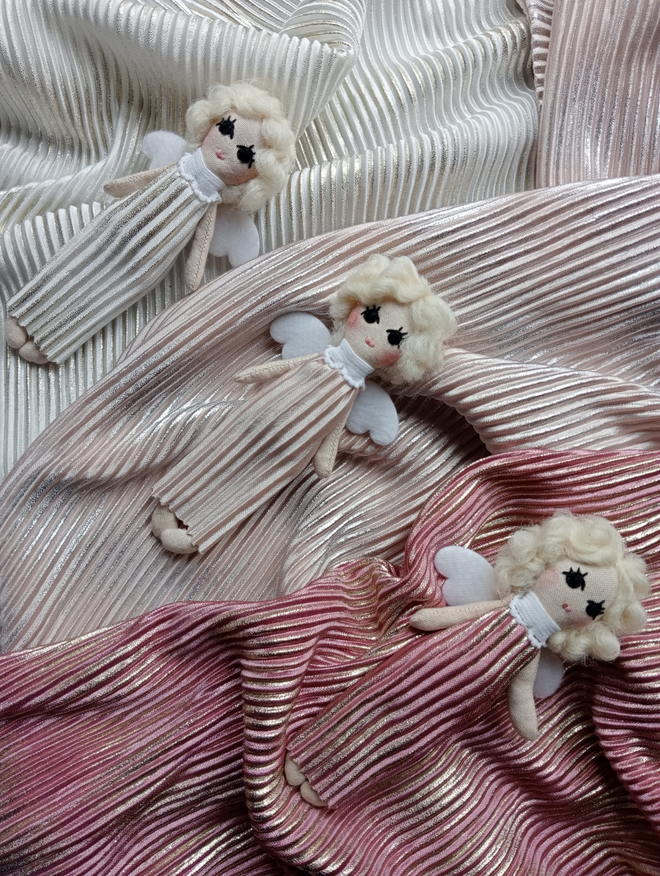 three tiny angel dolls all laying on three different colours of fabric. this fabric is the same as the gowns they are wearing. one is dusky pink one is champagne and one is pearly white. 