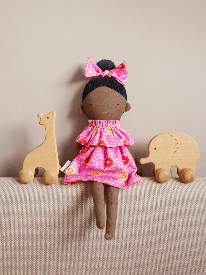 African-inspired handmade cloth doll with deep brown fabric skin, wearing a pink floral dress and matching bow