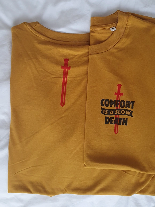  a yellow t-shirt with a black handprinted design on the front depicting a dagger and the phrase 'comfort is a slow death'