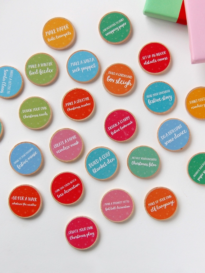 Twenty four wooden tokens with brightly coloured labels lay on a white surface.