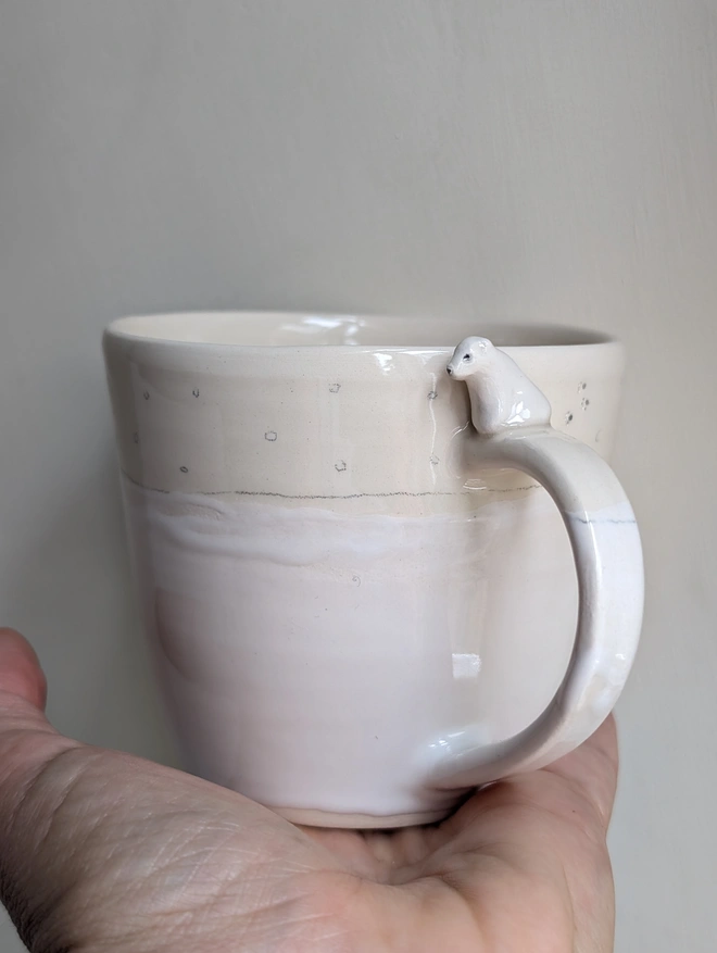 white cup with a ceramic polar bear sitting on the handle with tiny paw prints on the cup tiny hand painted snowflakes and white glaze held in a hand