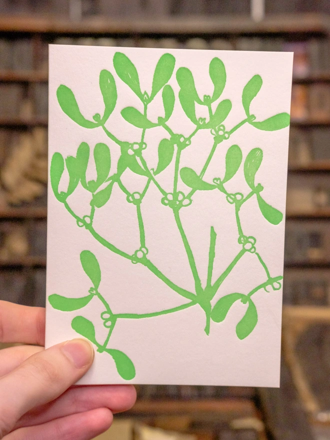 Card held up. Situation shot. Design on front visible. Monochrome green mistletoe design 