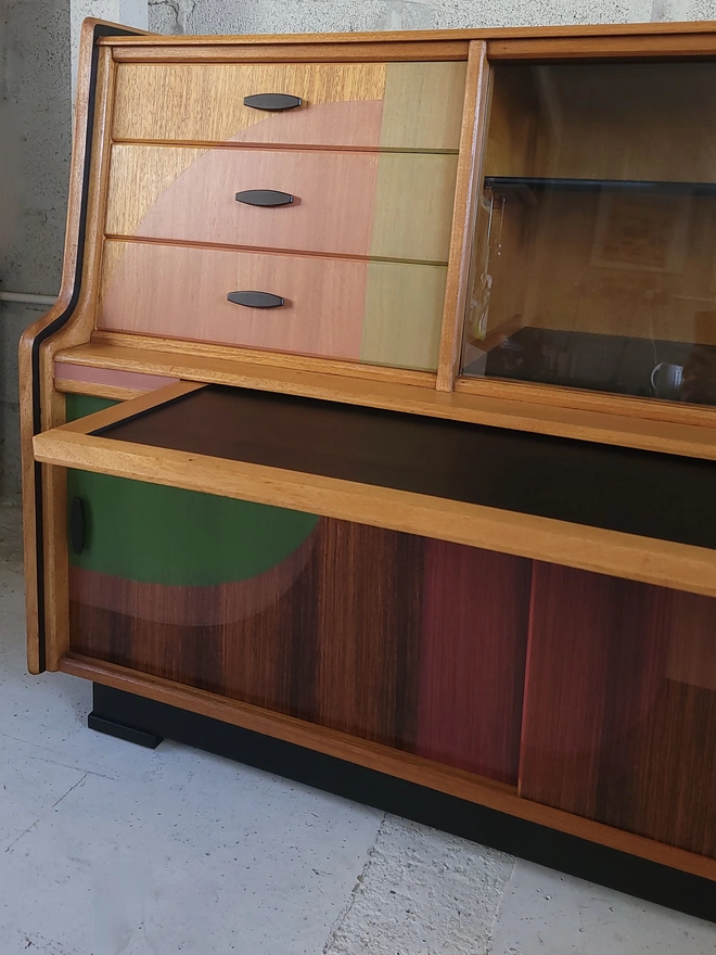 Teak mid-century sideboard drinks cabinet painted with green and pink geo shapes and a pull out shelf covered in black vinyl.