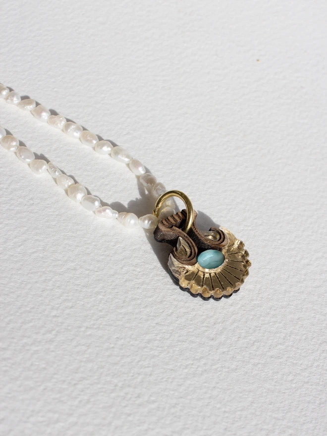 Pearl necklace with a shell shaped gold pendant & gemstone on a white background