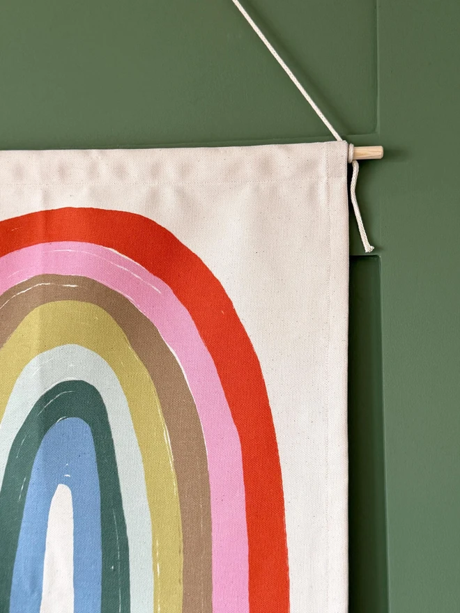 Cotton Pastel Rainbow Fabric Banner, against a green wall. 