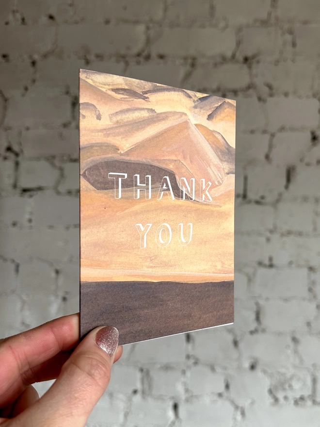a greetings card featuring an illustration of a sand dunes landscape with the text “thank you”