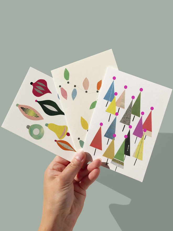 A set of three colourful modern Christmas cards featuring baubles, fairy lights and a forest of trees.