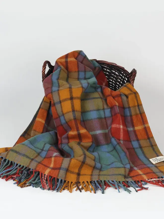 Buchanan Antique Picnic Blanket, a colourful picnic blanket sitting on top of a wooden basket on a white surface. 