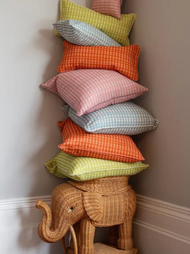 stack of multicoloured lali cushions on wicker elephant