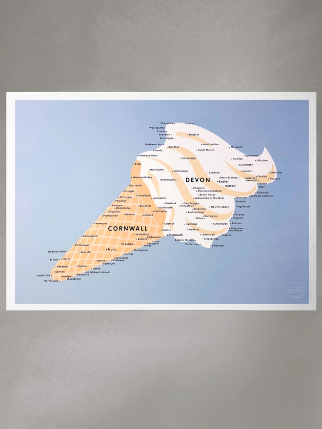  An ice cream that also happens to be a map of Devon and Cornwall, Cornwall being the cone and Devon the swirly ice cream. Little place names are dotted about in black. The whole ice cream is surrounded by sea. The print is flat laid on a grey board background.
