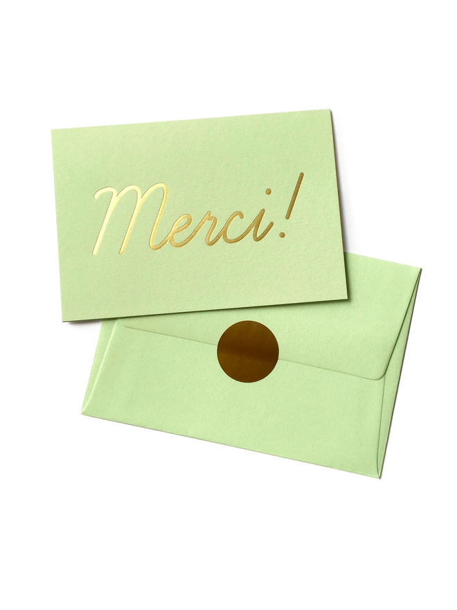 An elegant thank you card in mint green greeting card that says 'Merci!', wth an envelope that has a gold seal