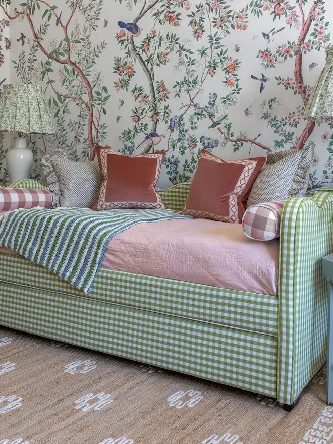 'the lochlan' green gingham upholstered children's bed. a green gingham sofa-style with a wavy headboard, photographed in a bedroom with patterned wallpaper.