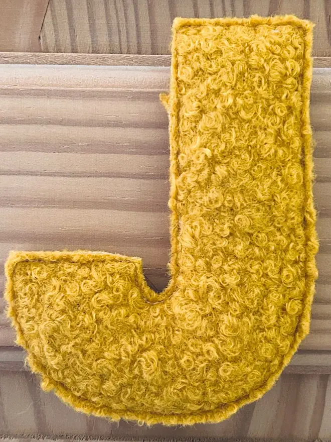 boucle letter bunting. a yellow fabric bunting letter 'J'.