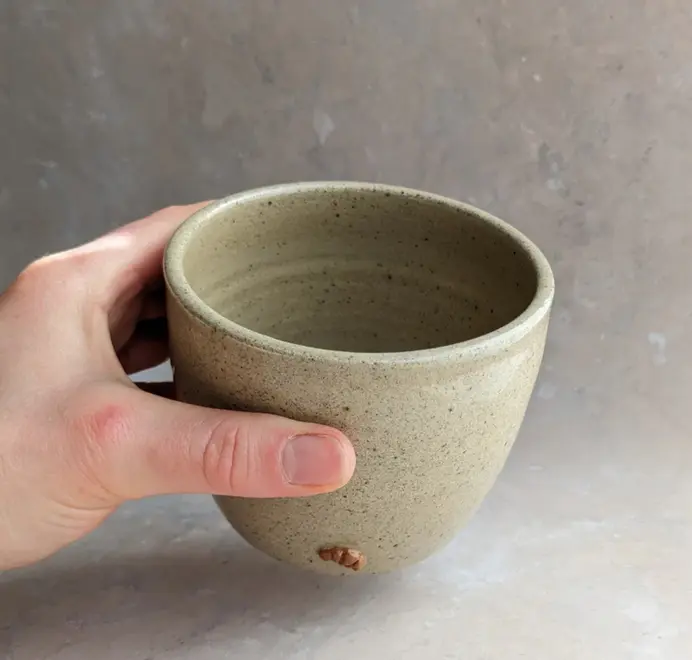 Biscuit colored croissant coffee cup with a subtle croissant design, placed against a grey marble background.