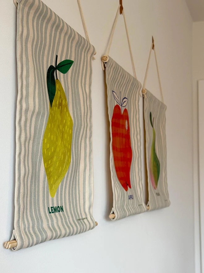 Cotton Lemon Wall Hanging, hanging on a white wall next to other fruit. 