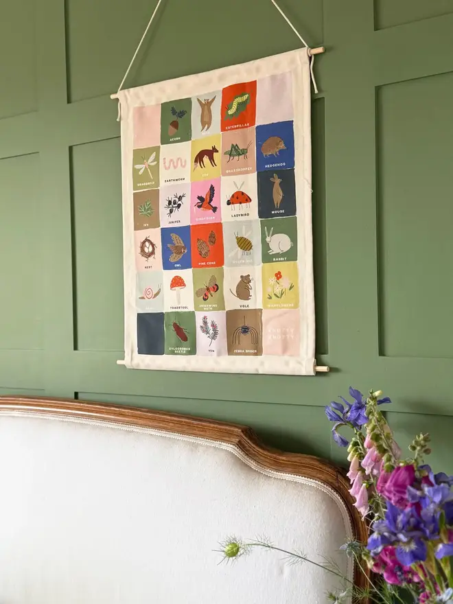 Rainbow Woodland Alphabet Fabric Banner, hanging in a green wall next to a bed. 