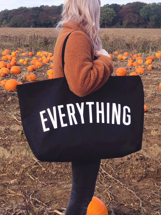 model holding an oversized black canvas tote bag with everything slogan in a pumpkin patch