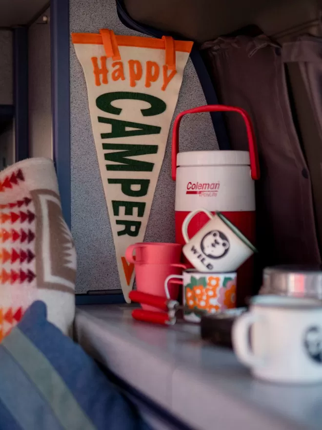 Happy camper flag hanging up in campervan with flask and mugs
