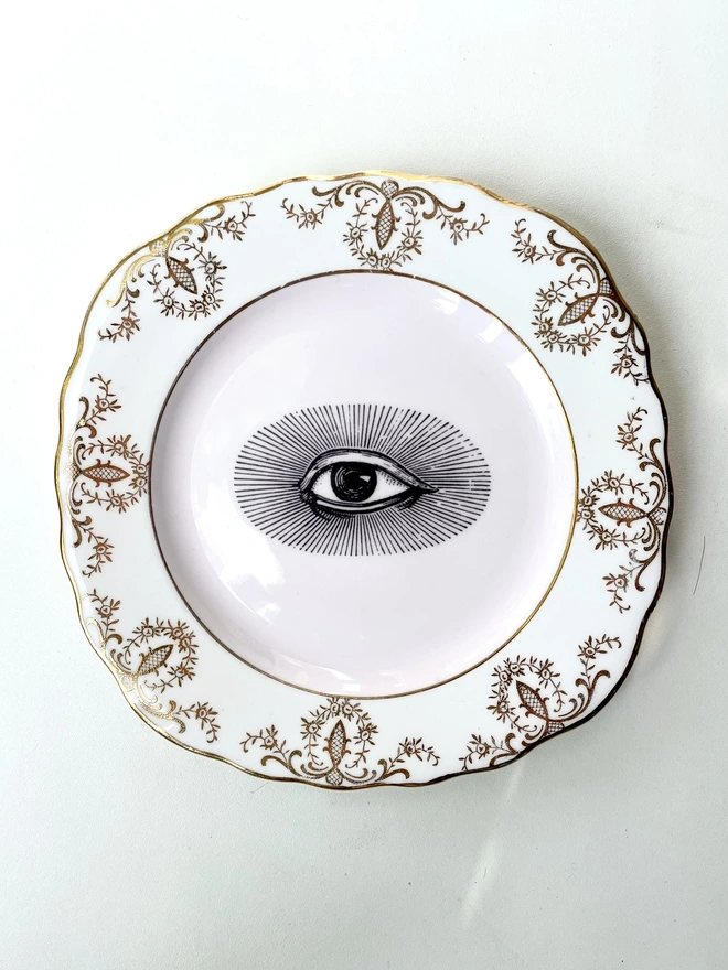 vintage plate with an ornate border, with a printed vintage illustration of an eye in the middle