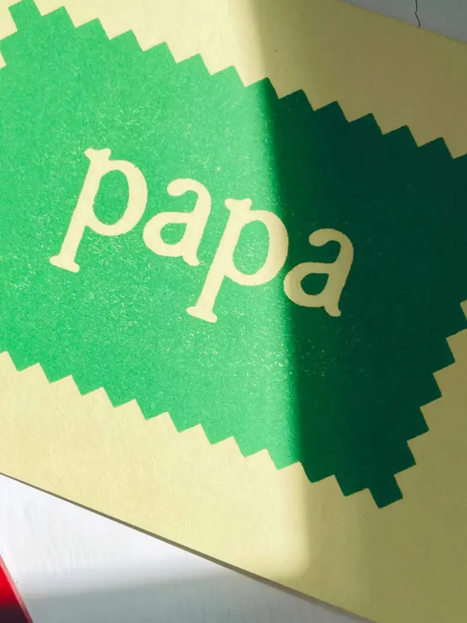 Hand-printed “Papa” card featuring cream lettering on a green zigzag-edged panel, set against a soft yellow background. 