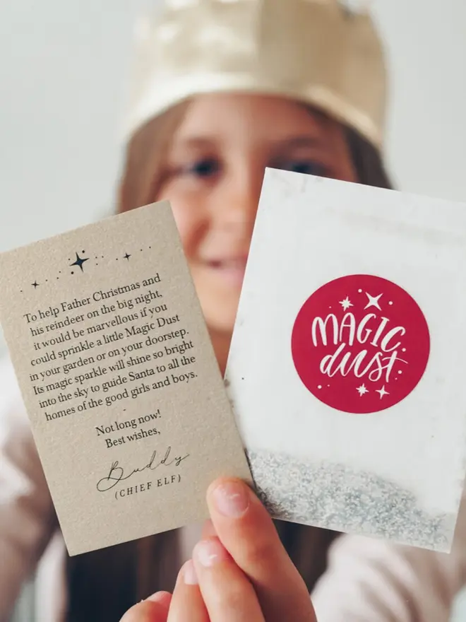 A child in a gold crown holds up the Magic Dust packet and a kraft Chief Elf note.