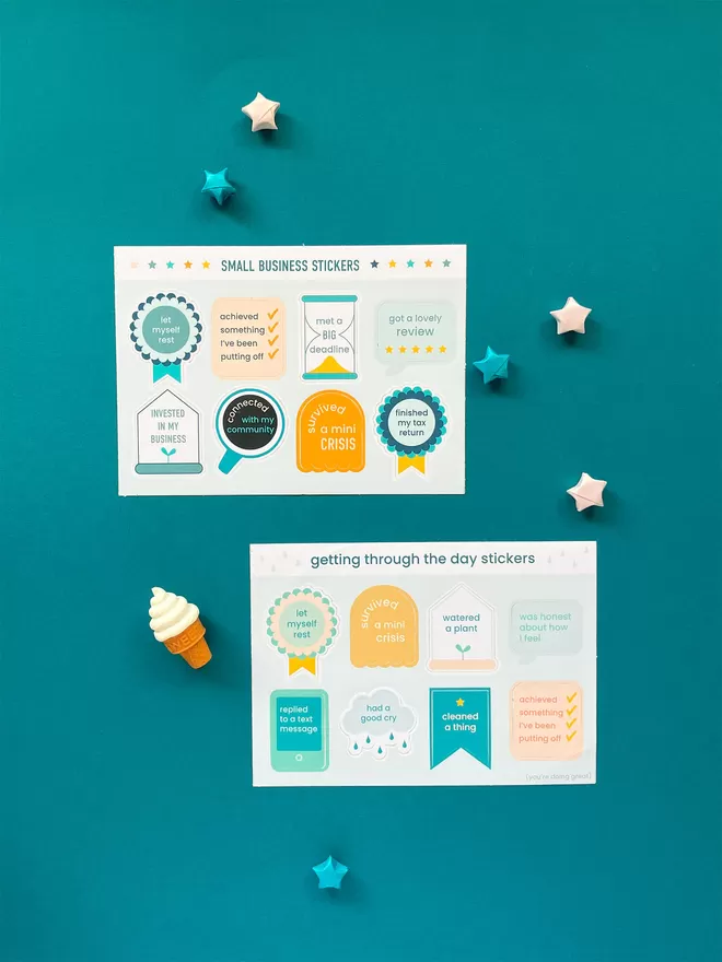 Two different sticker sheets sit on a turquoise blue background, surrounded by colourful paper stars