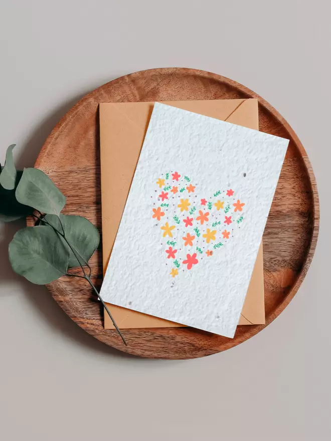 Seeded Paper Greeting Card with a heart made out floral illustrations in the centre on a wooden tray next to a Eucalyptus branch