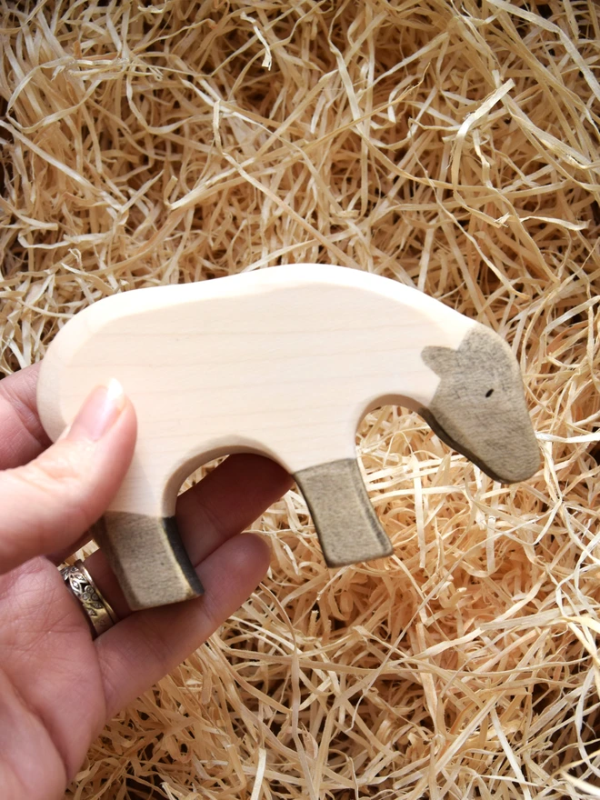 wooden toy black and white sheep being held in hand above woodwool