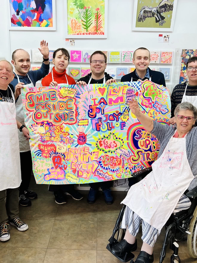 7 happy artists holding original Full of Joy artwork painted in bright colours with positive messages