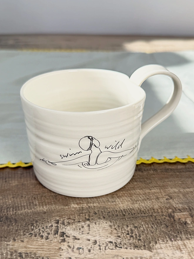 Handcrafted porcelain ‘Swim Wild’ mug – unique ceramic coffee cup for swimmers, nature lovers, and outdoor adventurers.
