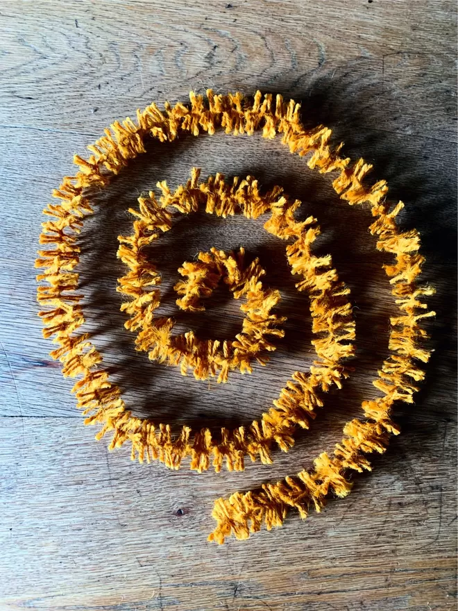 Warm Gold dyed jute string tinsel AKA Strinsel laid out in a spiral on an oak table