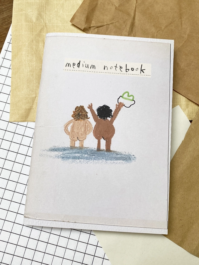 notebook with illustration of nude swimmers on desk with reclaimed sheets of paper surrounding.