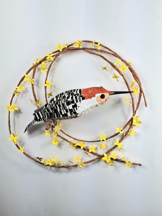 handmade sculpture of an orange bellied woodpecker, perched on a wreath of forsythia flowers