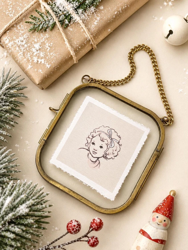 A portrait of a little girl drawn in a vintage story book style framed in a vintage brass and glass frame shown in a christmas flat lay