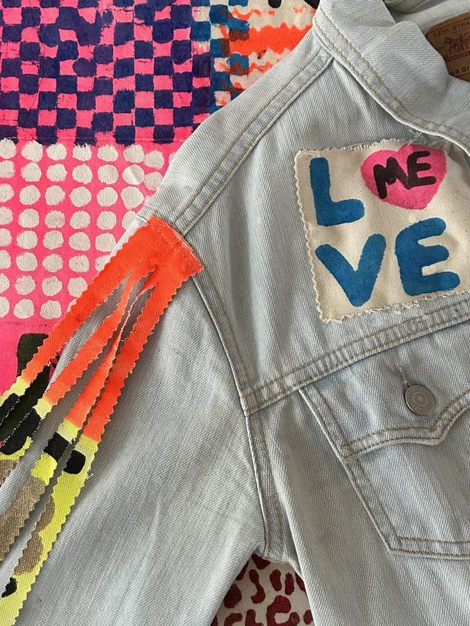 Denim jacket with love patch on it and tassled sleeves
