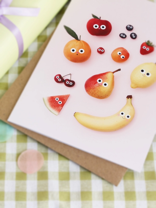 A detail shot of fruit friends card. Fruits with happy faces . on a green gingham tablecloth