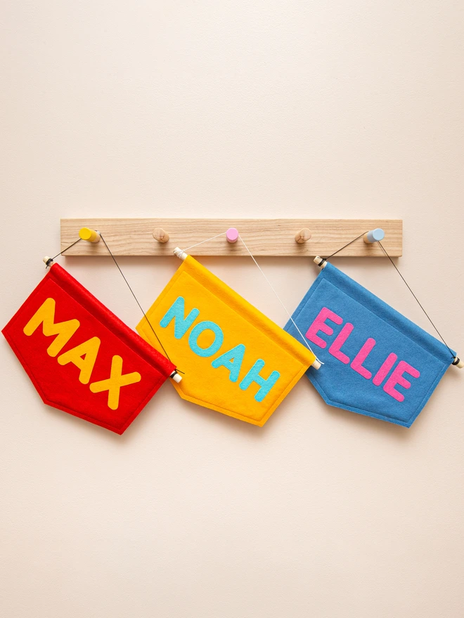 3 colourful, personalised felt name banners hanging from a pegrail.