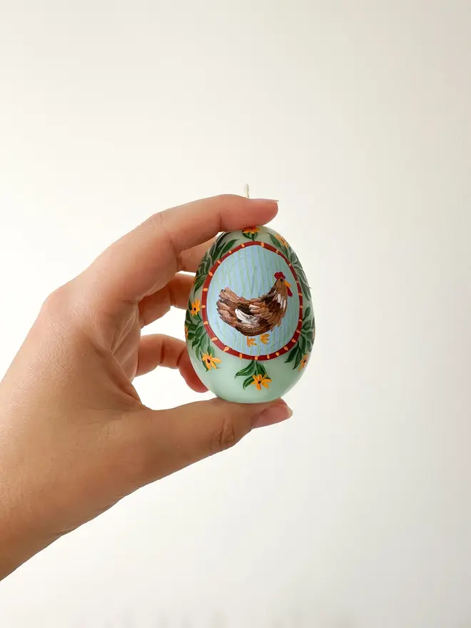 Hand Painted Easter Egg Candle Hen & Flowers, a woman holding an Easter egg candle against a plain backdrop. 