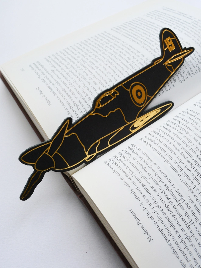 a leather spitfire shaped bookmark with gold detailing in an open book