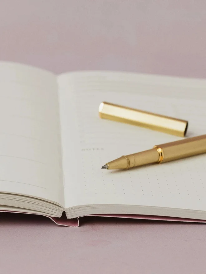 Close-up of an open Pinstripe Weekly Planner with a gold pen