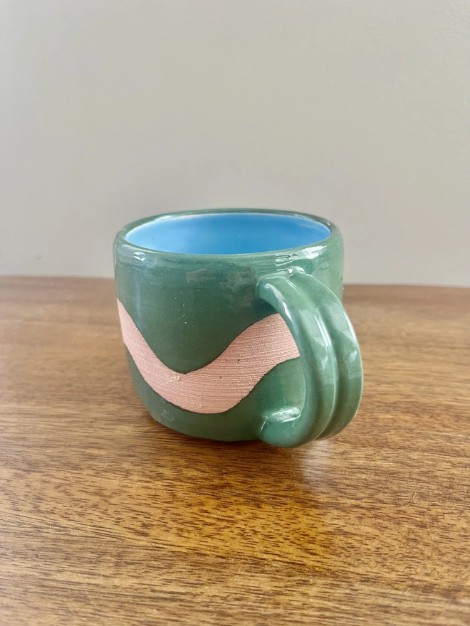Hand-thrown ceramic flat white mug with forest green glaze, exposed clay wave design, bright blue interior and chunky ribbed handle, handmade by Hannah Inskip Pottery.
