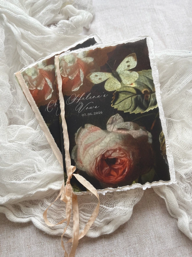 2 x blank handmade paper vow booklets with a vellum cover printed with roses and butterflies. Very romantic and tied with blush silk effect ribbon