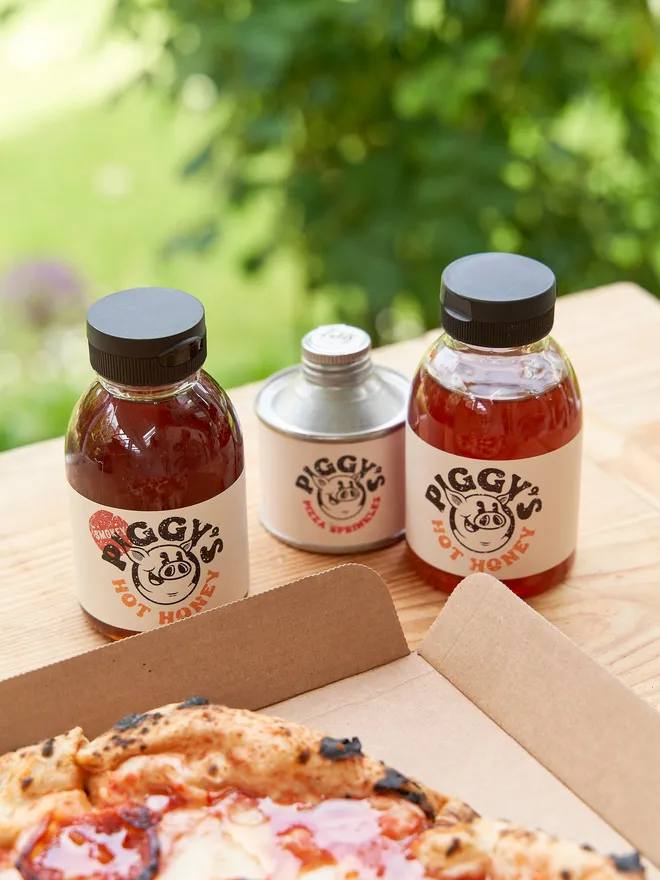 Piggy's Hot Honey- held up against a pizza in the garden 