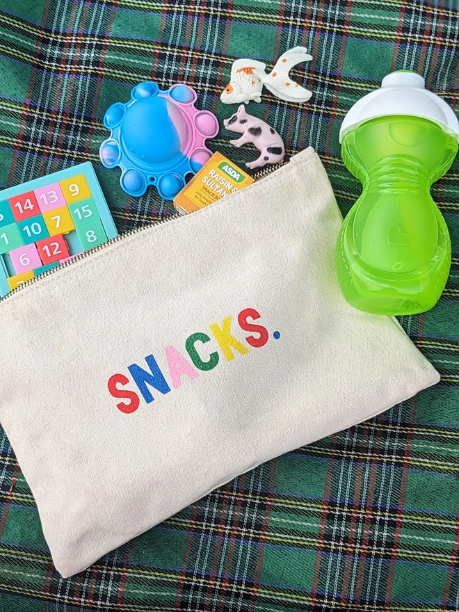 A canvas pouch on a checked blanket with multi coloured 'Snacks slogan